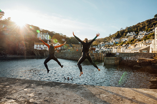 Two people leaping into the water at a sunlit harbour